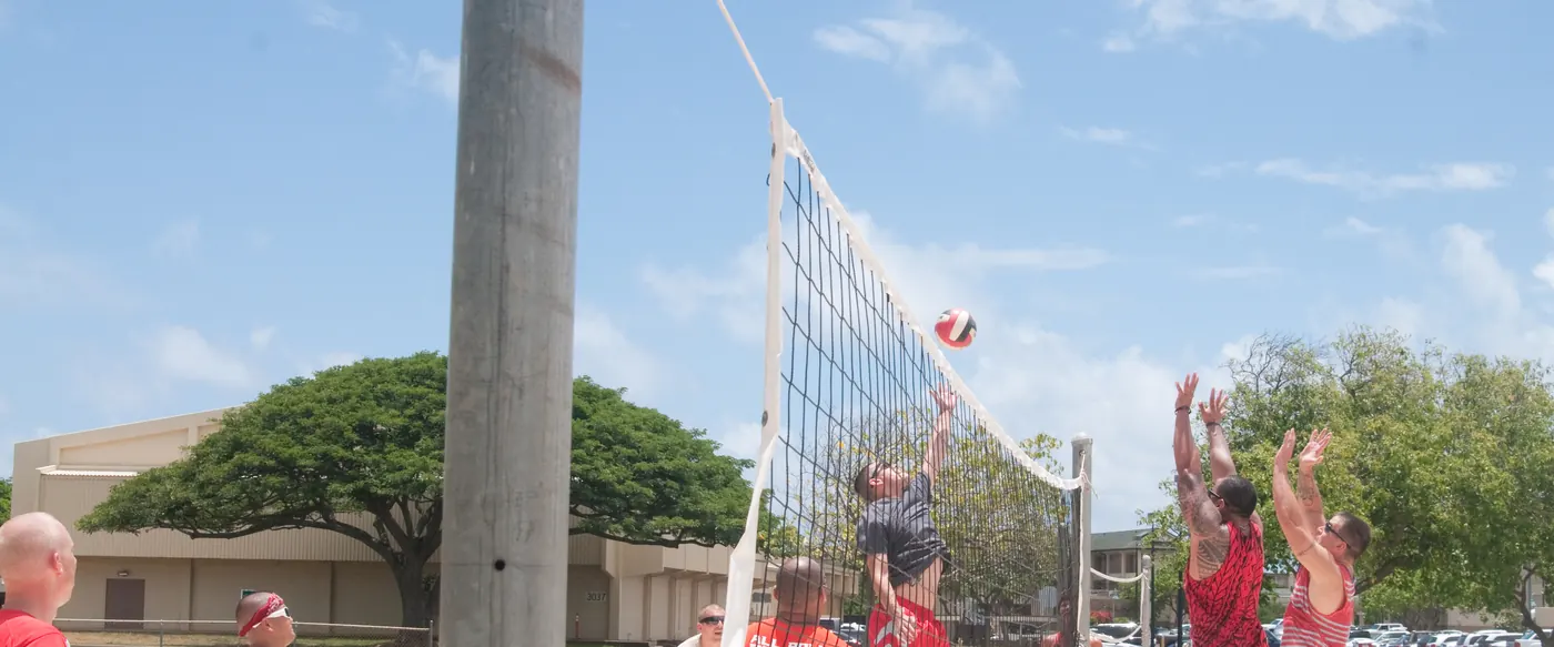 Players reaching for the ball at the net during a sand volleyball game